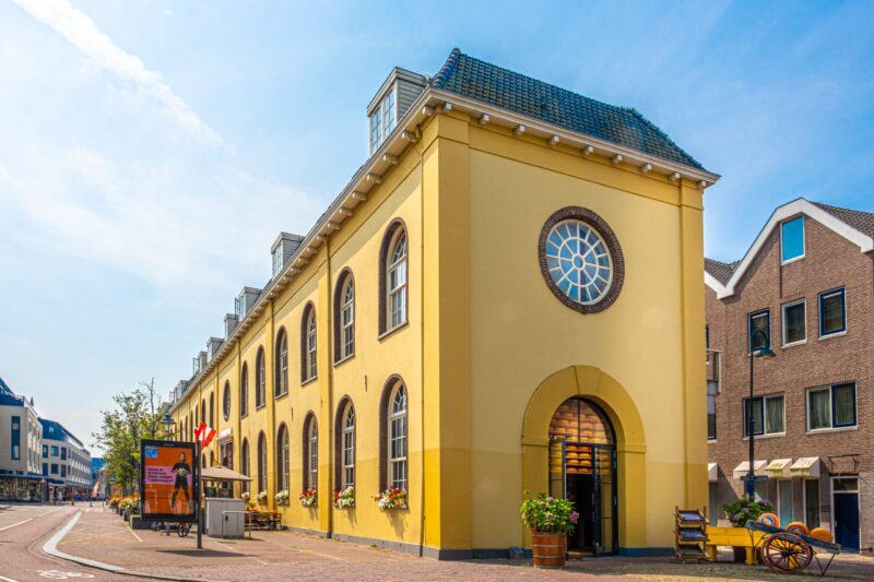 Foto van het gele pand van de Gouda Cheese Experience van buiten tegen een blauwe lucht.