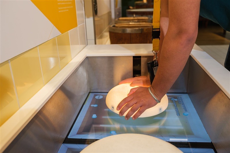 Bezoeker draait een kaaswiel op een interactieve tafel tijdens de Gouda Cheese Experience.
